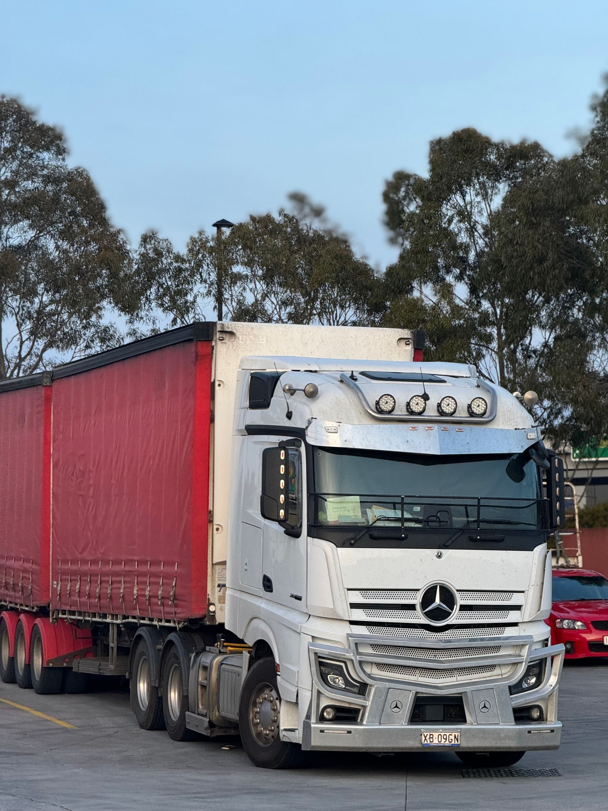 White freight truck with a red trailer at a logistics hub